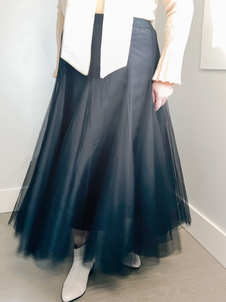 My Maiden Tulle Skirt in Black is a skirt with flowing layers of fine tulle that is lightweight of midi length with a slip underneath. Anne, an Asian woman, @PurposeInView is wearing the skirt. Camera view is from the waist down.