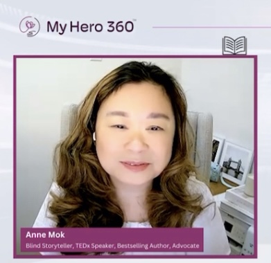 The image appears to be a screenshot from a virtual interview or discussion on the My Hero 360 platform. The screen is divided into two frames. On the left side is Anne Mok, labeled as "Blind Storyteller, TEDx Speaker, Bestselling Author, Advocate." She is smiling softly, wearing a light top, with her wavy hair falling around her shoulders. Behind her is a cozy background featuring a chair and a desk with books and décor. On the right side is Jillian Comstock, the "My Hero 360™ Host." Jillian has long, light brown hair and a warm smile. She is wearing a dark top, and her background is a blurred indoor space, focusing on her face. At the top of the image, the My Hero 360™ logo is displayed, and the design includes soft purple and white accents, with small icons above the participants representing storytelling and mindfulness